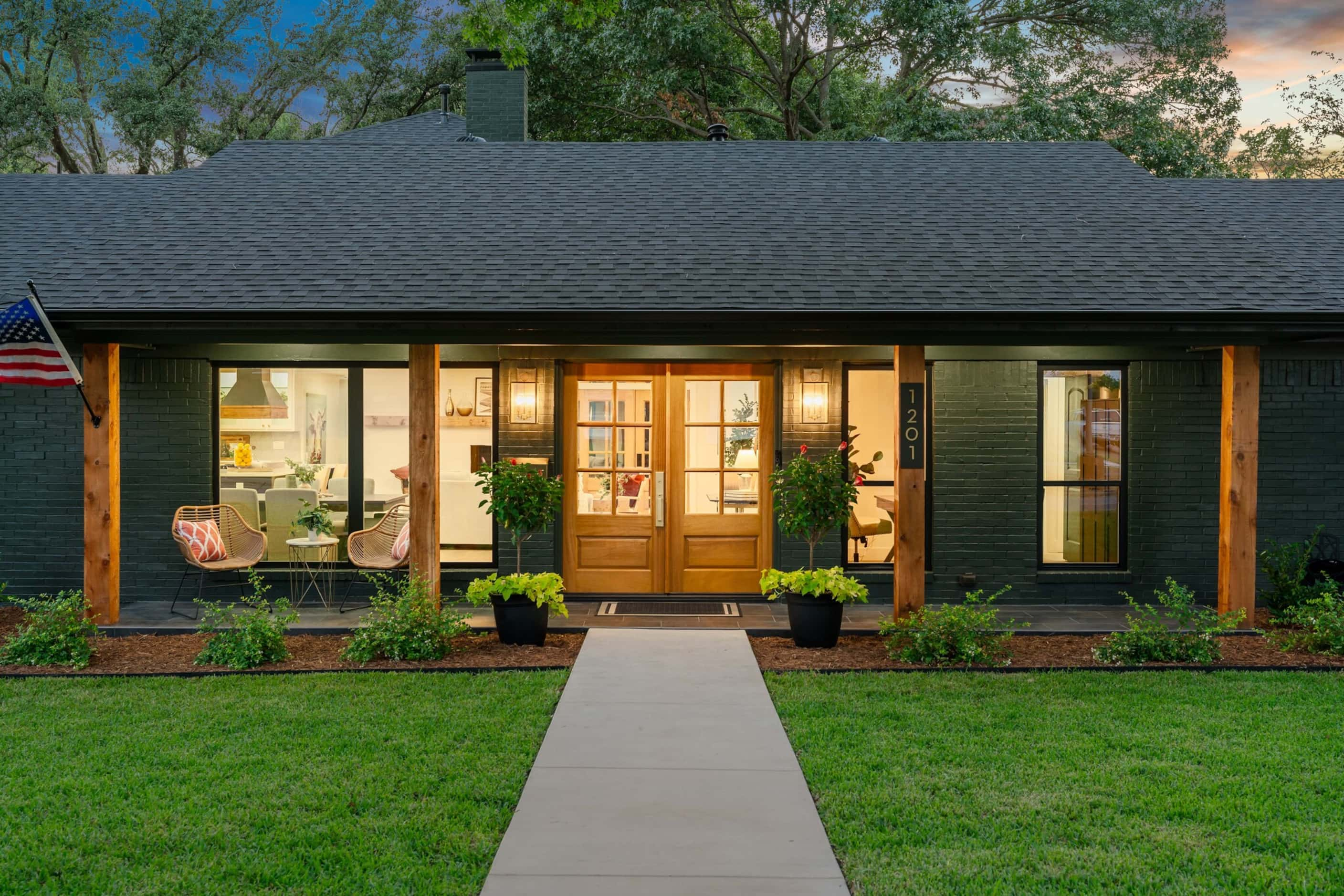 Dark green house with long front porch has multiple windows, double front doors and wood...