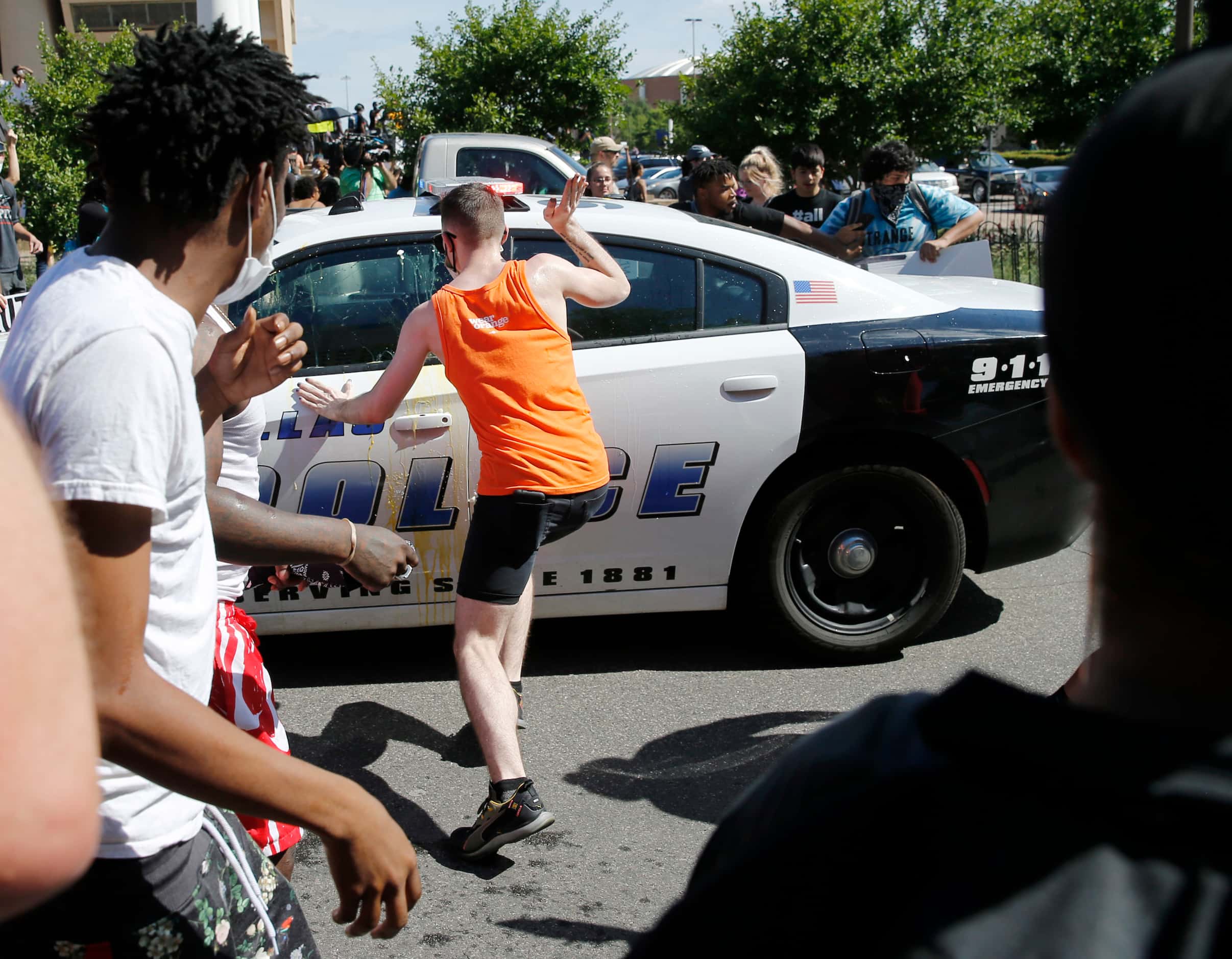 A protester hits a Dallas police car as it backs up on Young Street during a protest against...