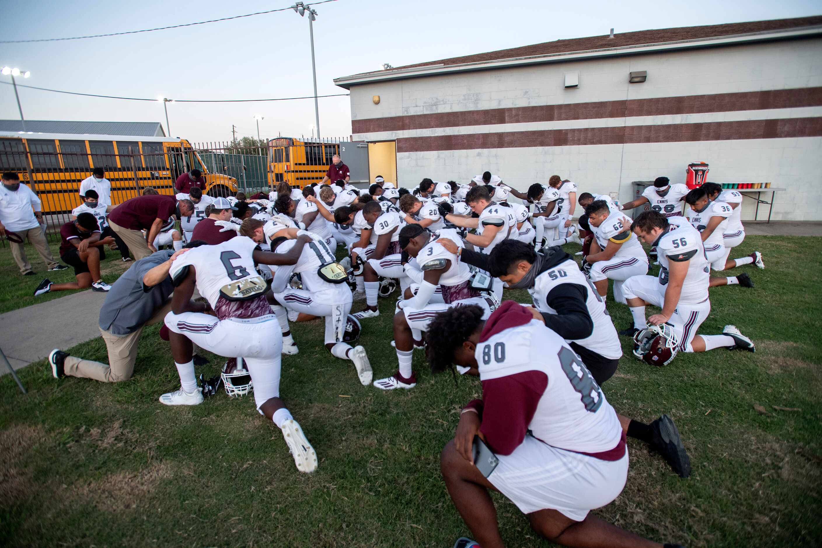 Ennis players and coaches pray before a high school football game against Red Oak on Friday,...
