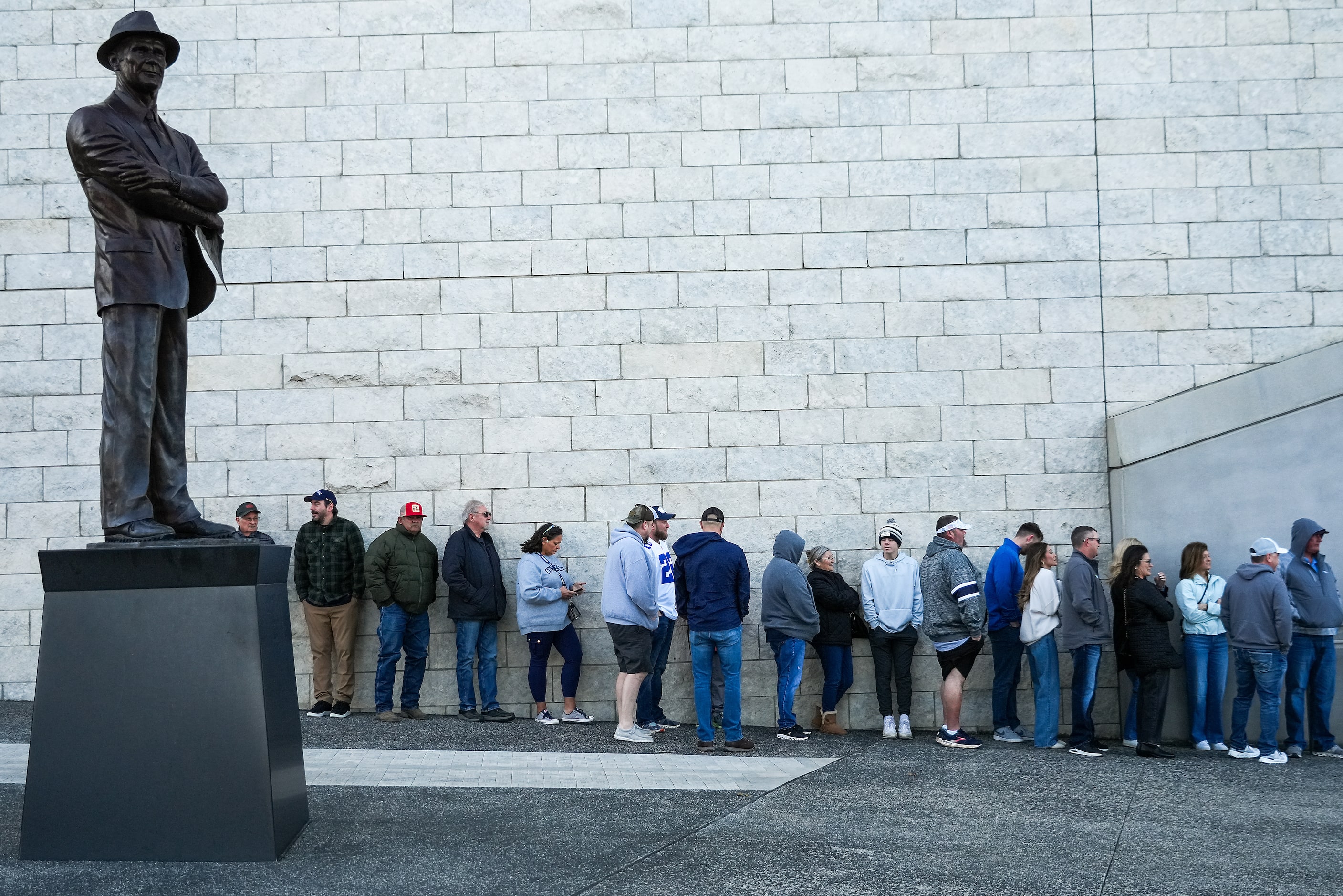 Fans try to find shelter from a cold wind as they wait for the gates to open before an NFL...