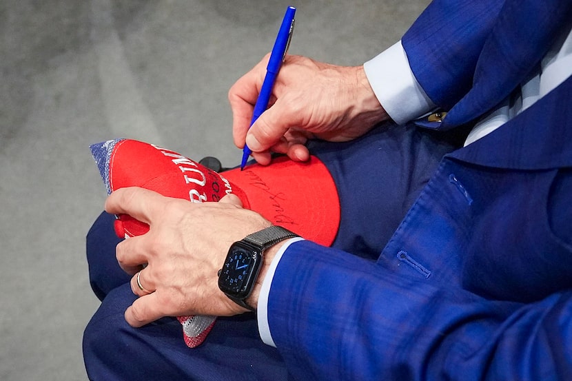 Texas Gov. Greg Abbott autographs a Donald Trump campaign hat for a supporter at a campaign...