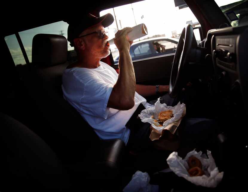 Parked in his Jeep, Ray Pena of Dallas enjoys a Miller Lite with a No. 5 double patty burger...
