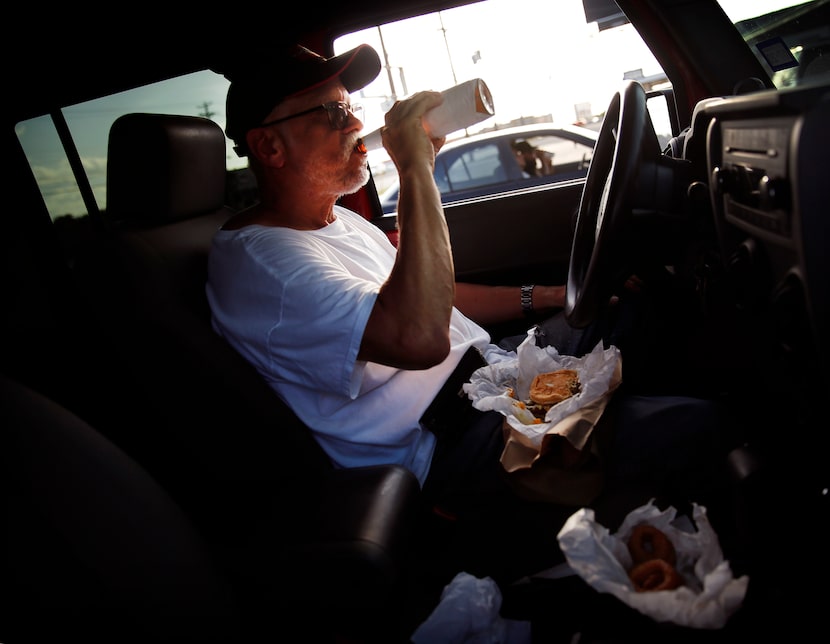 Parked in his Jeep, Ray Pena of Dallas enjoys a Miller Lite with a No. 5 double patty burger...