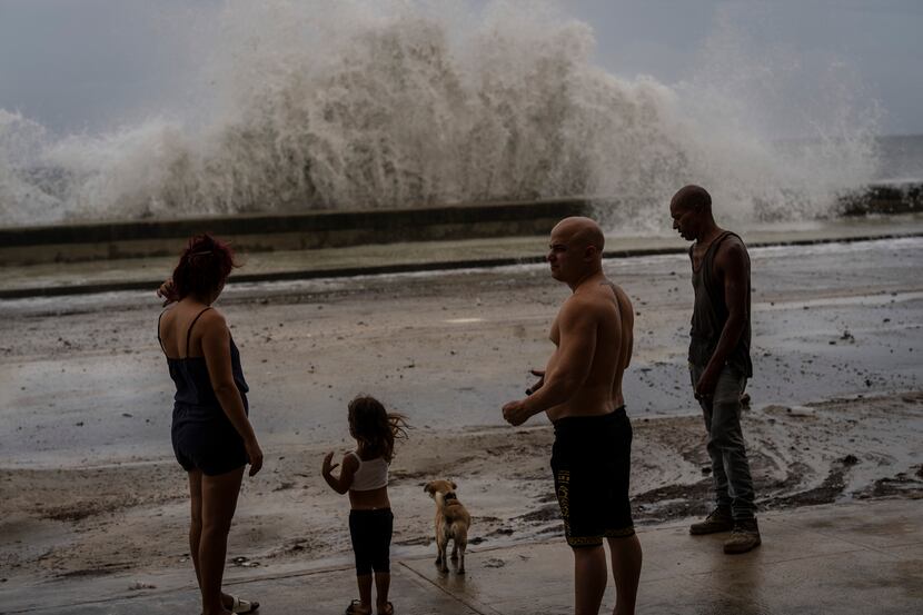 People stand along a waterfront as huge waves crash against a seawall in the wake of...