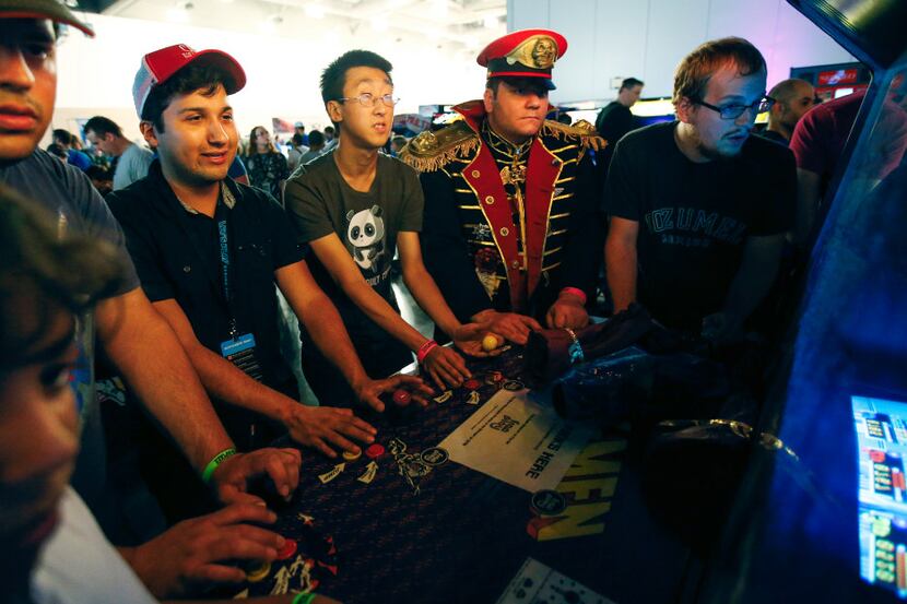 Six players gather around an arcade game during the Let's Play Gaming Expo at the Irving...