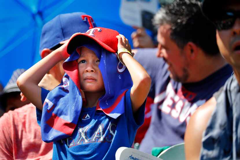 Young Texas Rangers fan Ripken Echols takes cover from the searing sun as he watches his...