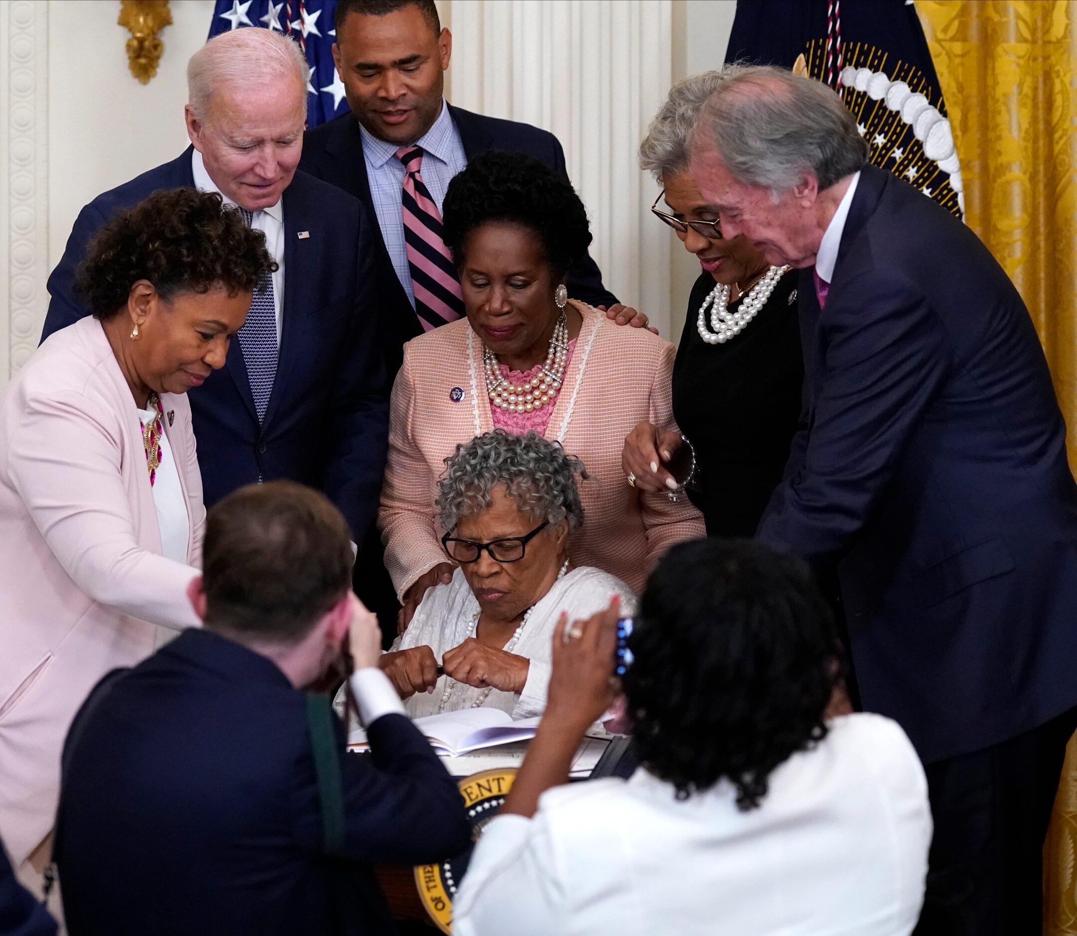 People take photos as Opal Lee holds a pen and is seated where President Joe Biden signed...