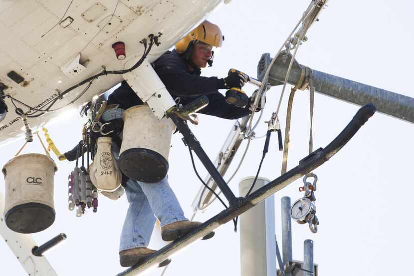 A helicopter lineman for an Oncor contractor works on transmission lines near Royal Lane at...
