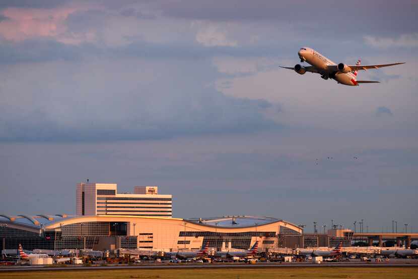 An American Airlines jet takes flight from DFW International Airport against a dramatic sunset.