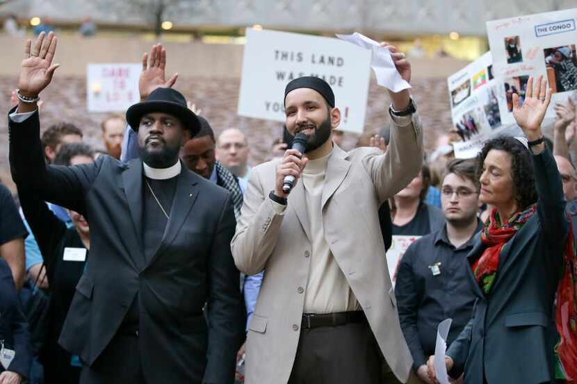 Iman Omar Suleiman, center, raises his hand with Rabbi Nancy Kasten, right, and the Rev....