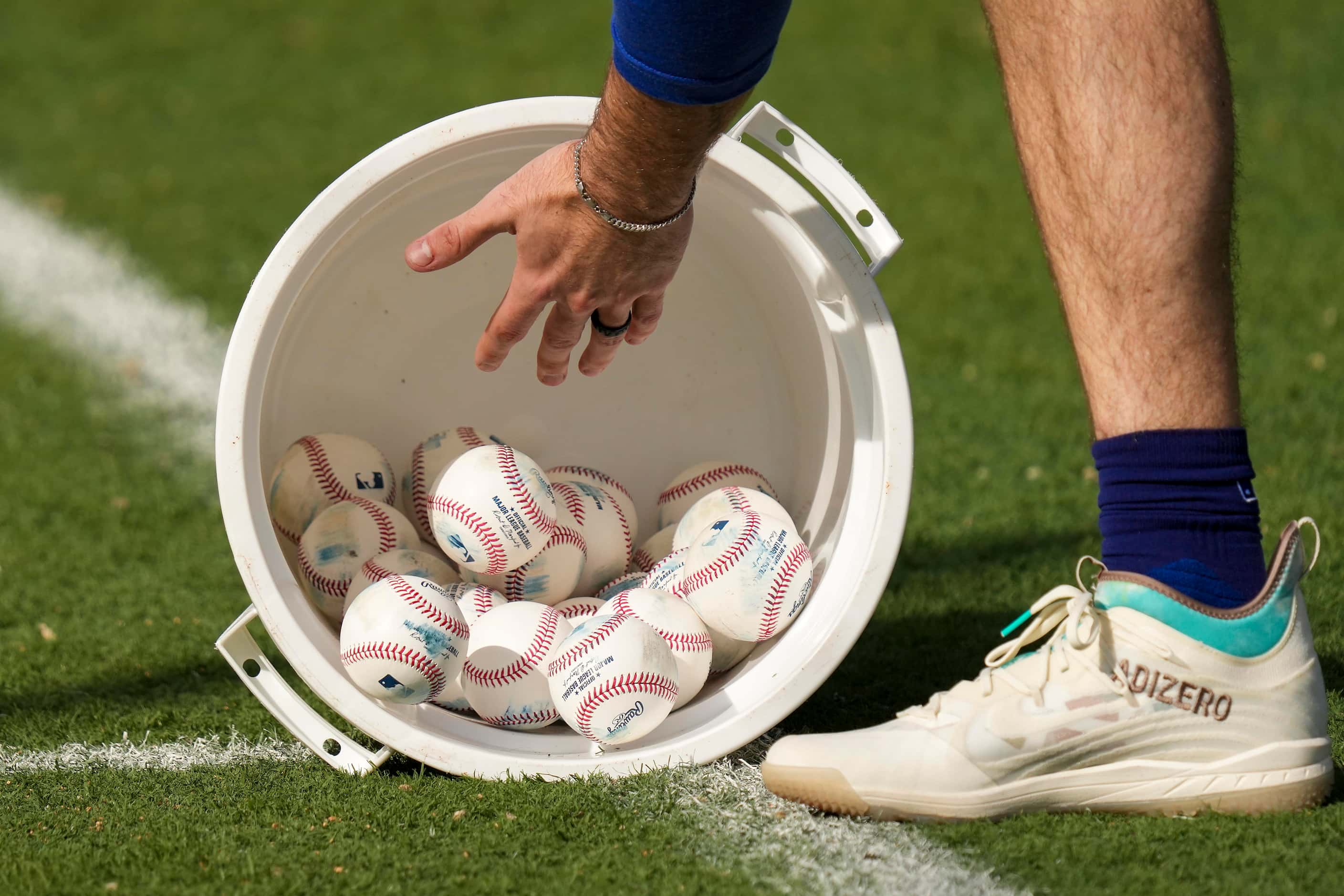 Texas Rangers outfielder Evan Carter fills up a bucket of practice baseballs after a drill...