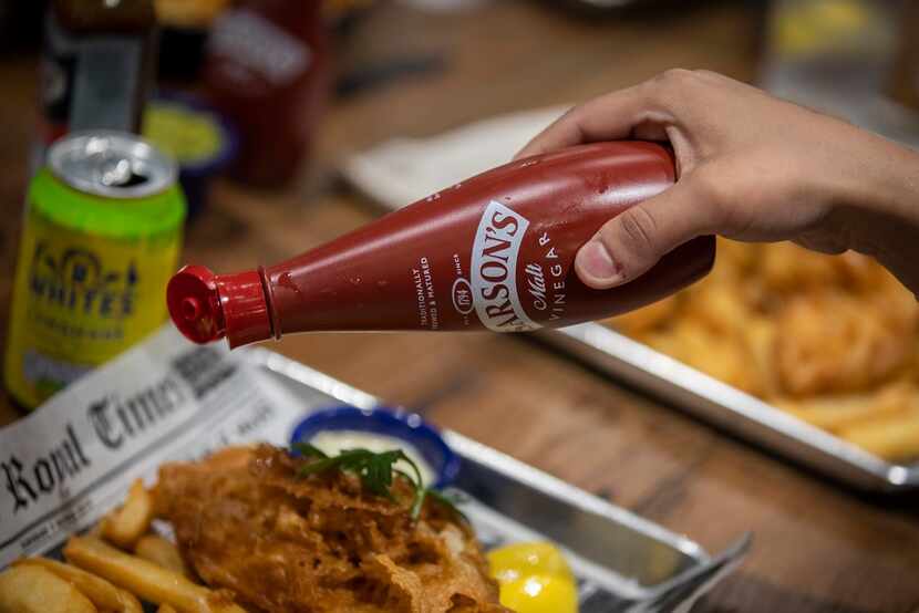 A diner pours Sarson's malt vinegar on her order of fish and chips at Fish & Fizz.