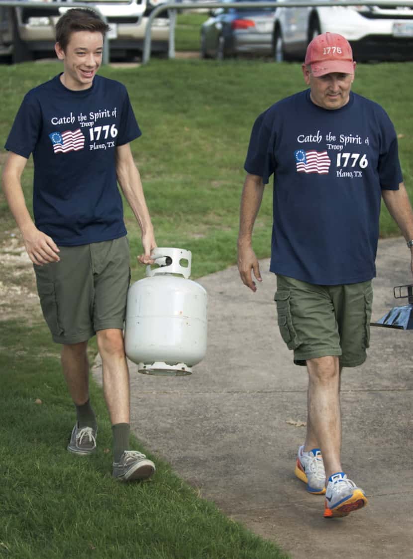 Bradley Davis and Scoutmaster Jeff Joiner carry grilling equipment to a Boy Scout picnic at...