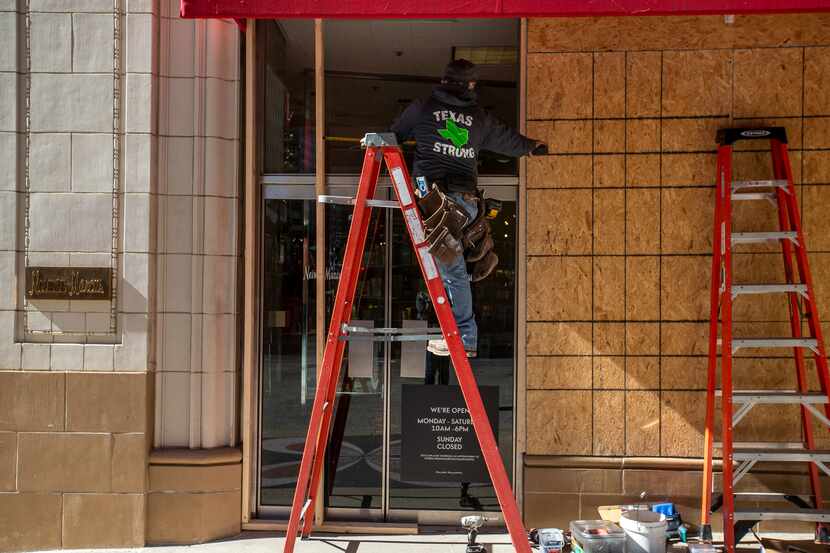 Manuel González, an employee at County Glass LLC, helps to board up the storefront of Neiman...