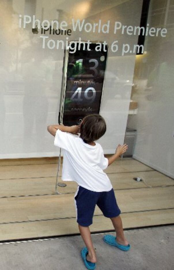 A youngster watches the countdown clock as he and others wait in line outside the Apple...