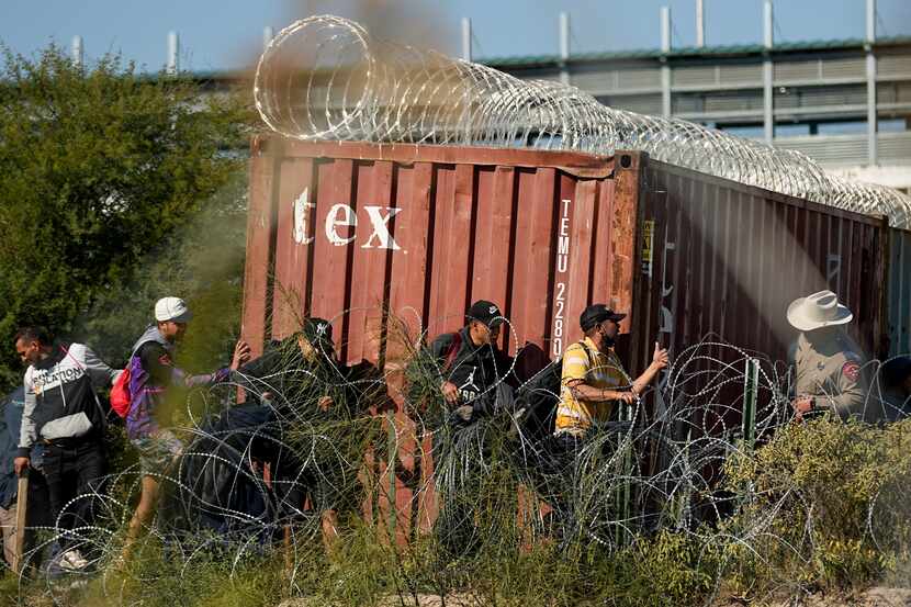 A Texas Department of Public Safety official, right, looks on as migrants walk near a rail...