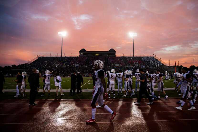 Allen football players walk along the sideline as rain falls and the sun sets during the...