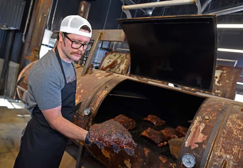 Drew Lindsey, a pit crew member, shows off one of the beef ribs being cooked inside a large...