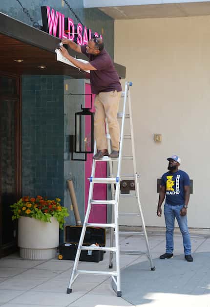 Mamun Rashid (on ladder) and Price Maniungu install the new signage at Wild Salsa in...