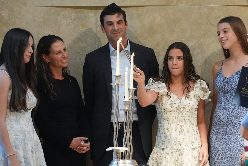  Quinn Schimel, second from left, lights a Shabbat candle as she stands with her family...