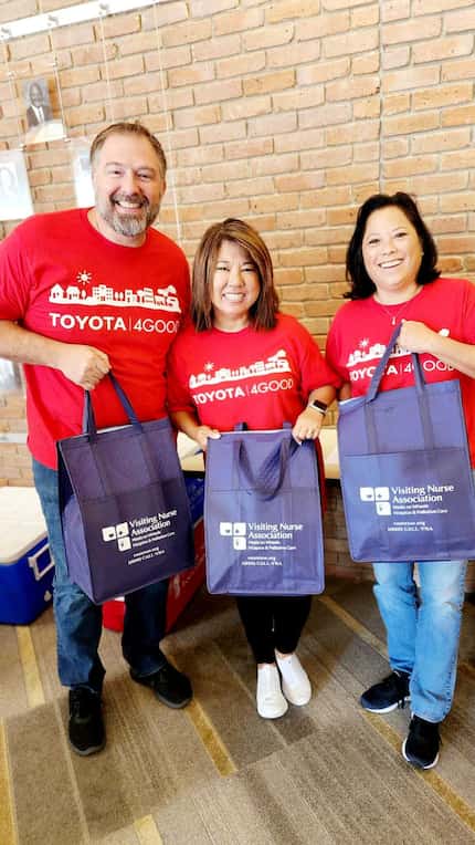 Three smiling volunteers in red Toyota t-shirts holding bags containing meals to be...