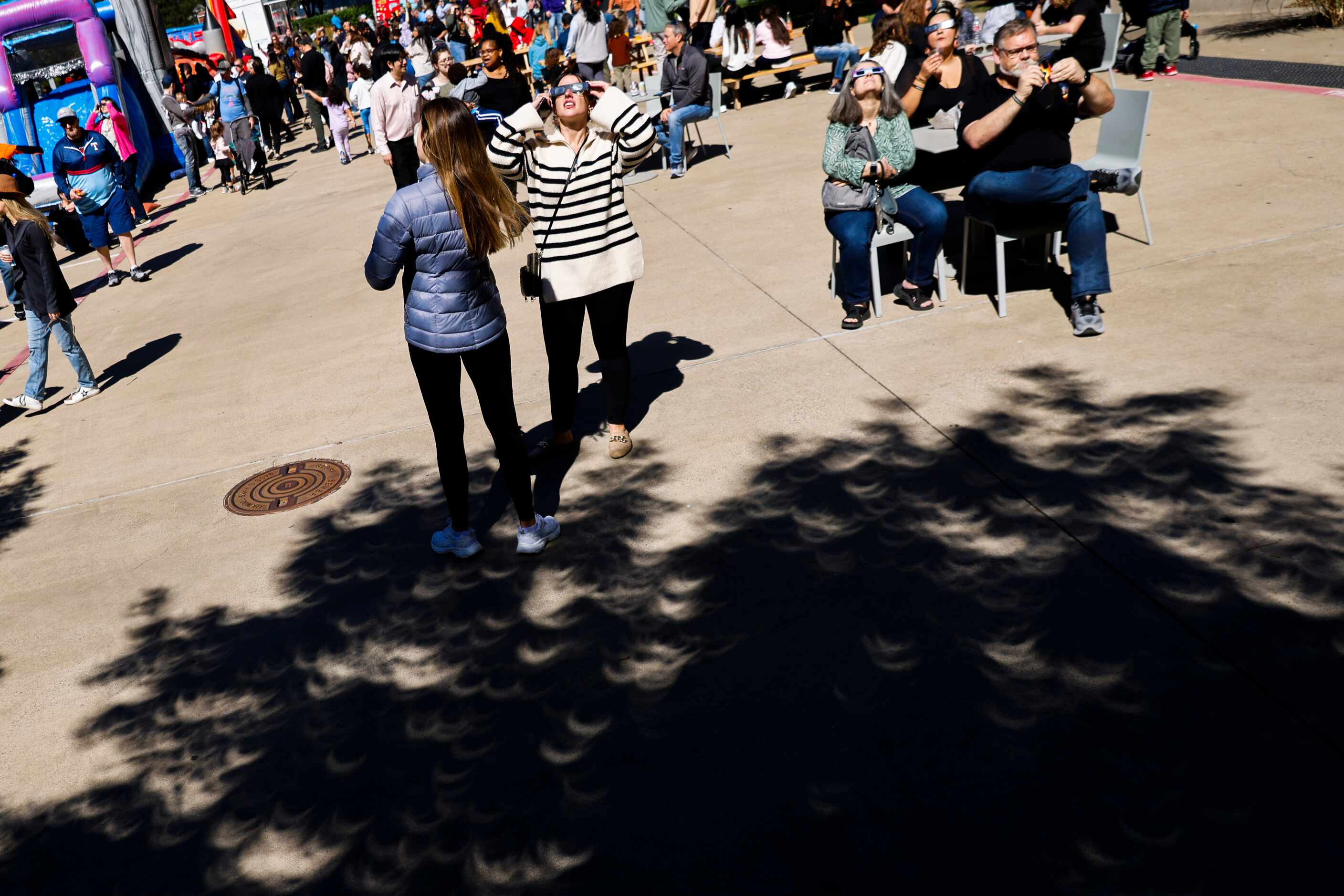 People watch the annular solar eclipse as it cast little eclipse shadows on the ground on...