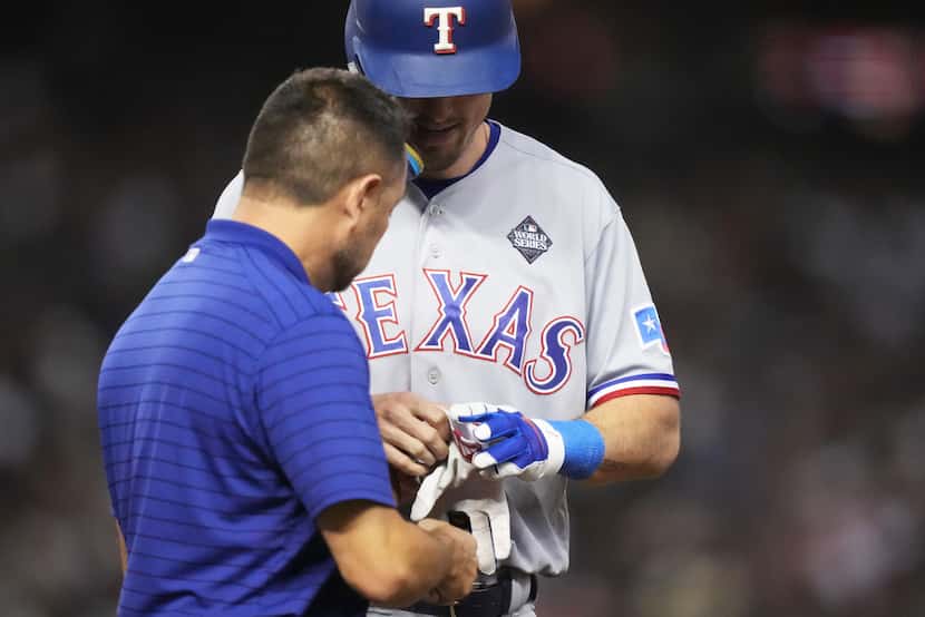 A Texas Rangers’ trainer checks on Evan Carter after being hit on his right hand by a pitch...