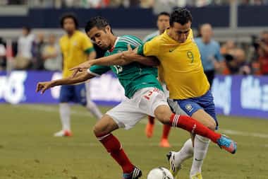 Forward Leandro Damiao (9) of Brazil and defenseman Severo Meza (13) of Mexico battle for...