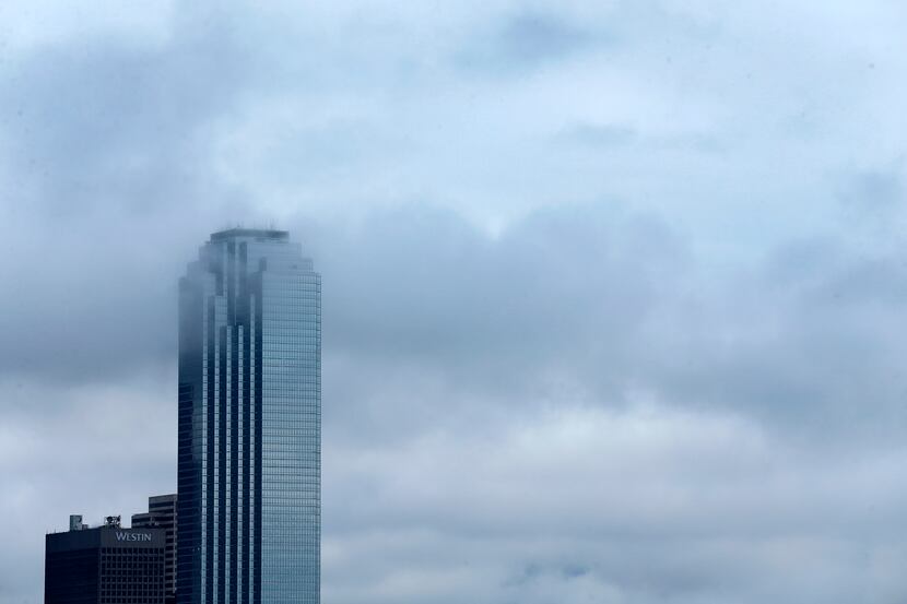 Lingering clouds drifted around the Bank of America building in downtown Dallas as a cold...