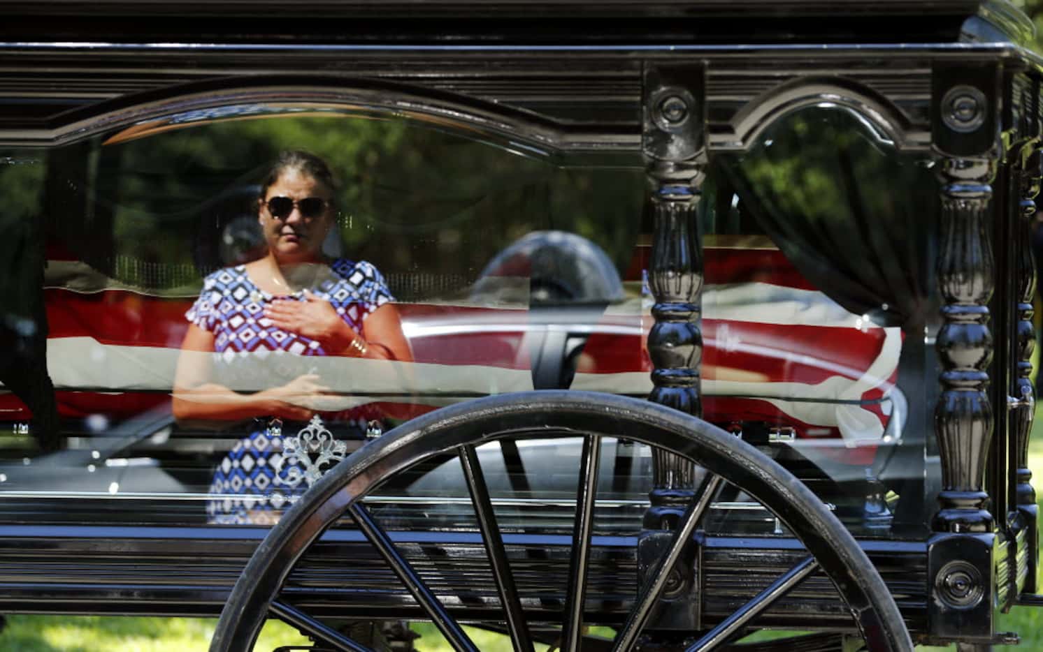 In the reflection of the horse-drawn caisson, a Smith family member places her hand over her...