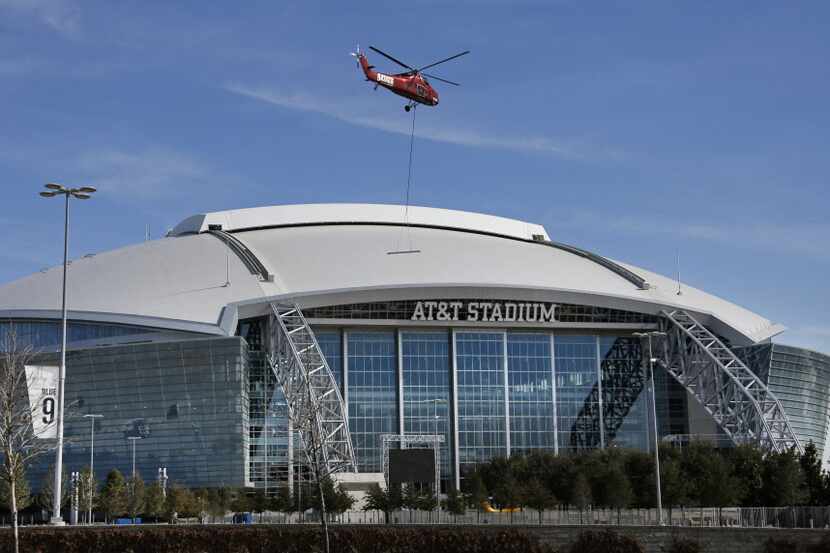 A helicopter hovers over the parking lot as it transports items to the roof of AT&T Stadium...