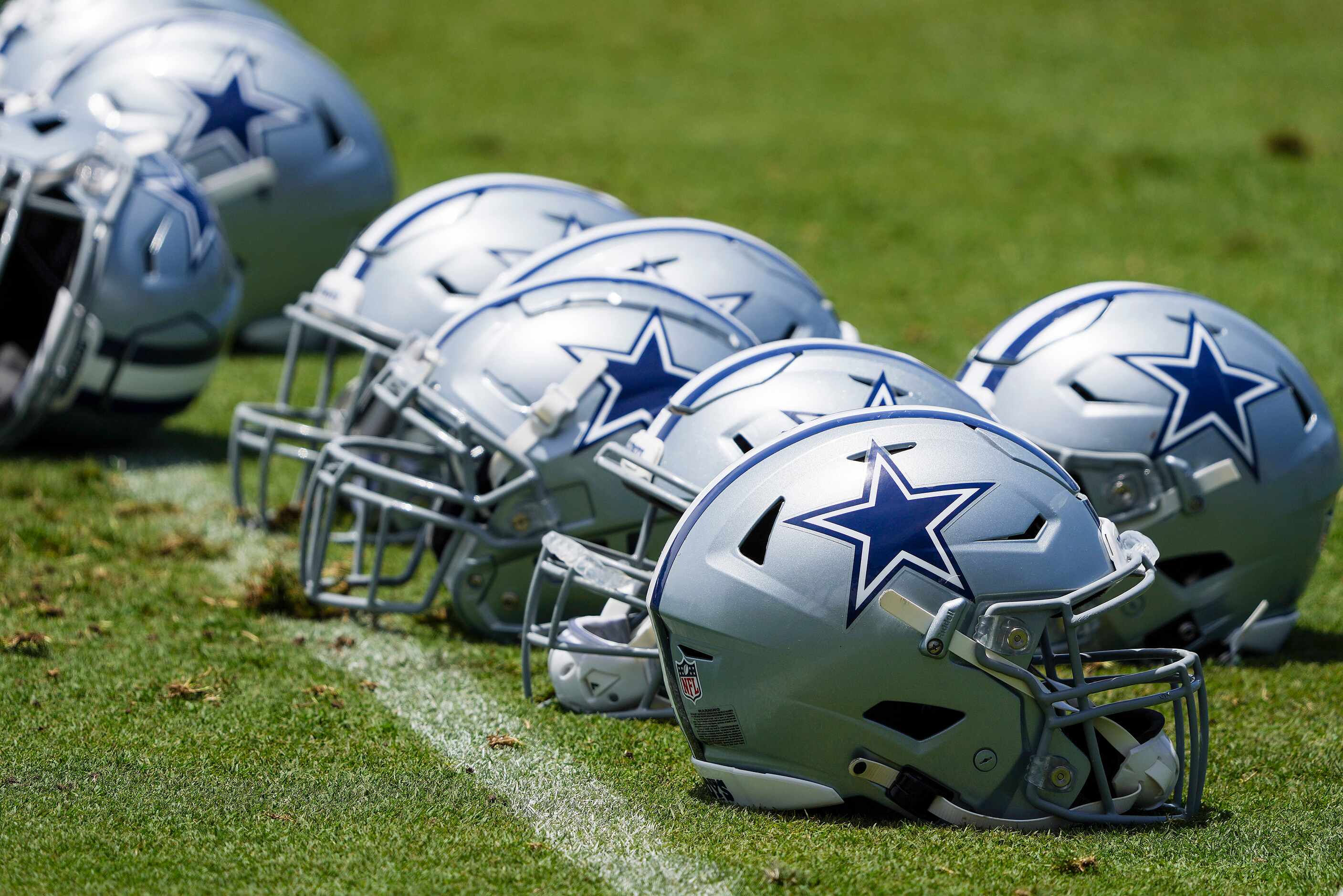 A row of Dallas Cowboys helmets rests on the field during the first practice of the team’s...