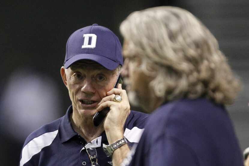 Dallas Cowboys owner Jerry Jones talks on the phone as he looks at defensive coordinator Rob...