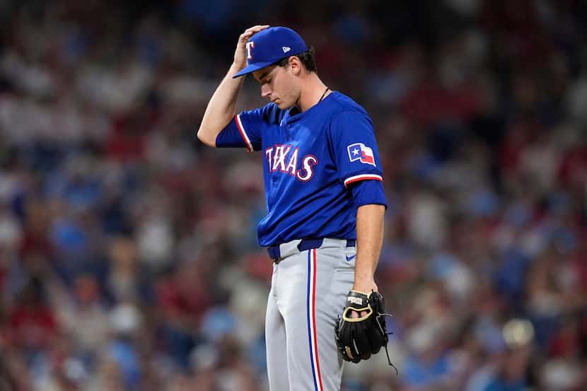 Texas Rangers pitcher Cole Winn adjusts his hat after giving up a single to Philadelphia...