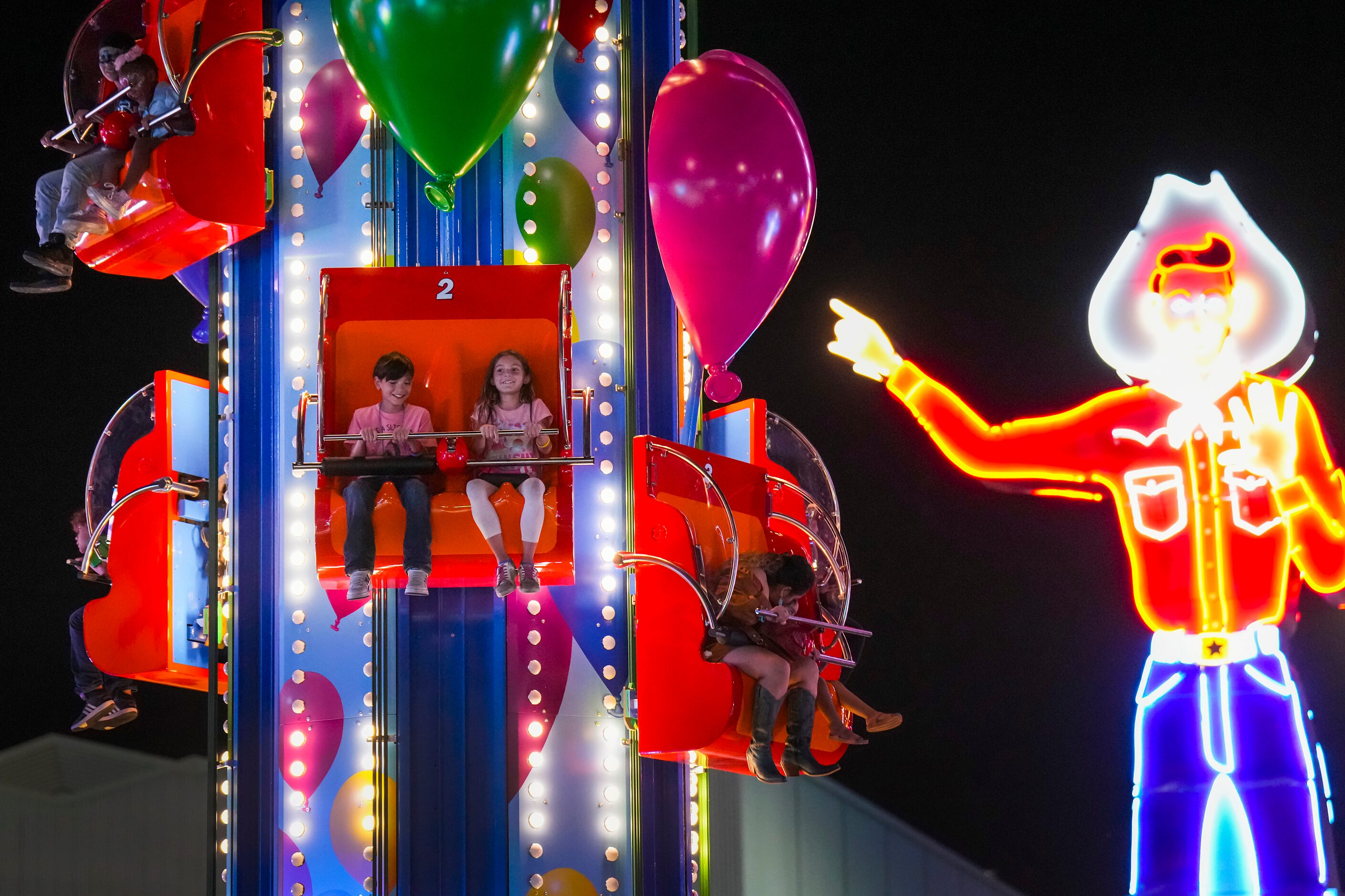 Neon Big Tex points toward youngsters on a ride on the midway on opening night at the State...