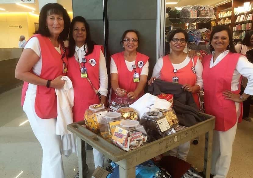A group photo of The Golden Girls wearing red vests and standing with a cart full of snacks....