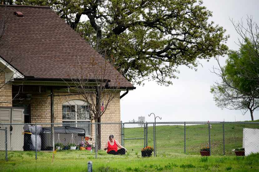 A woman pulls weeds in her yard outside one of the cottage duplex units at Texas Masonic...