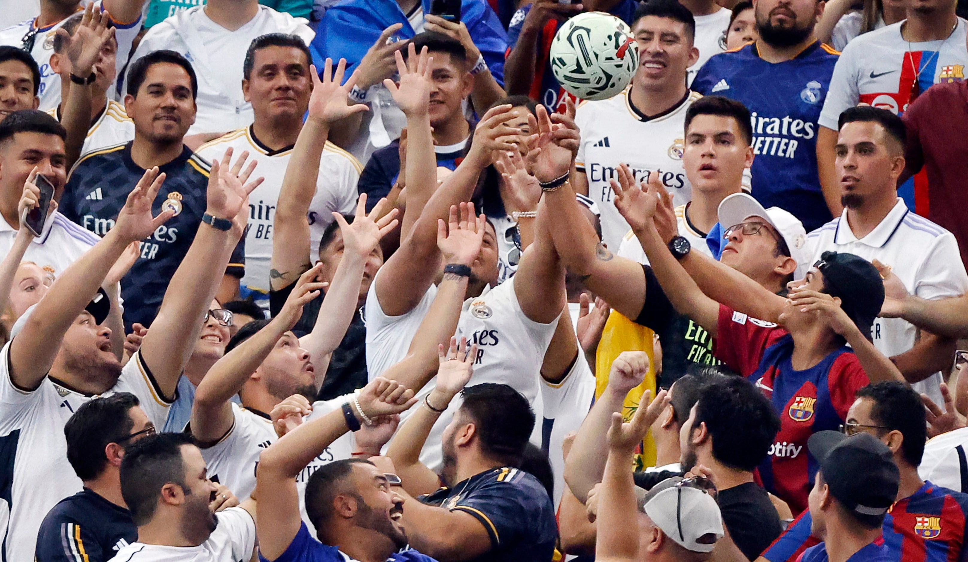 Real Madrid fans reach for a game ball that was kicked into the lower seating area during...