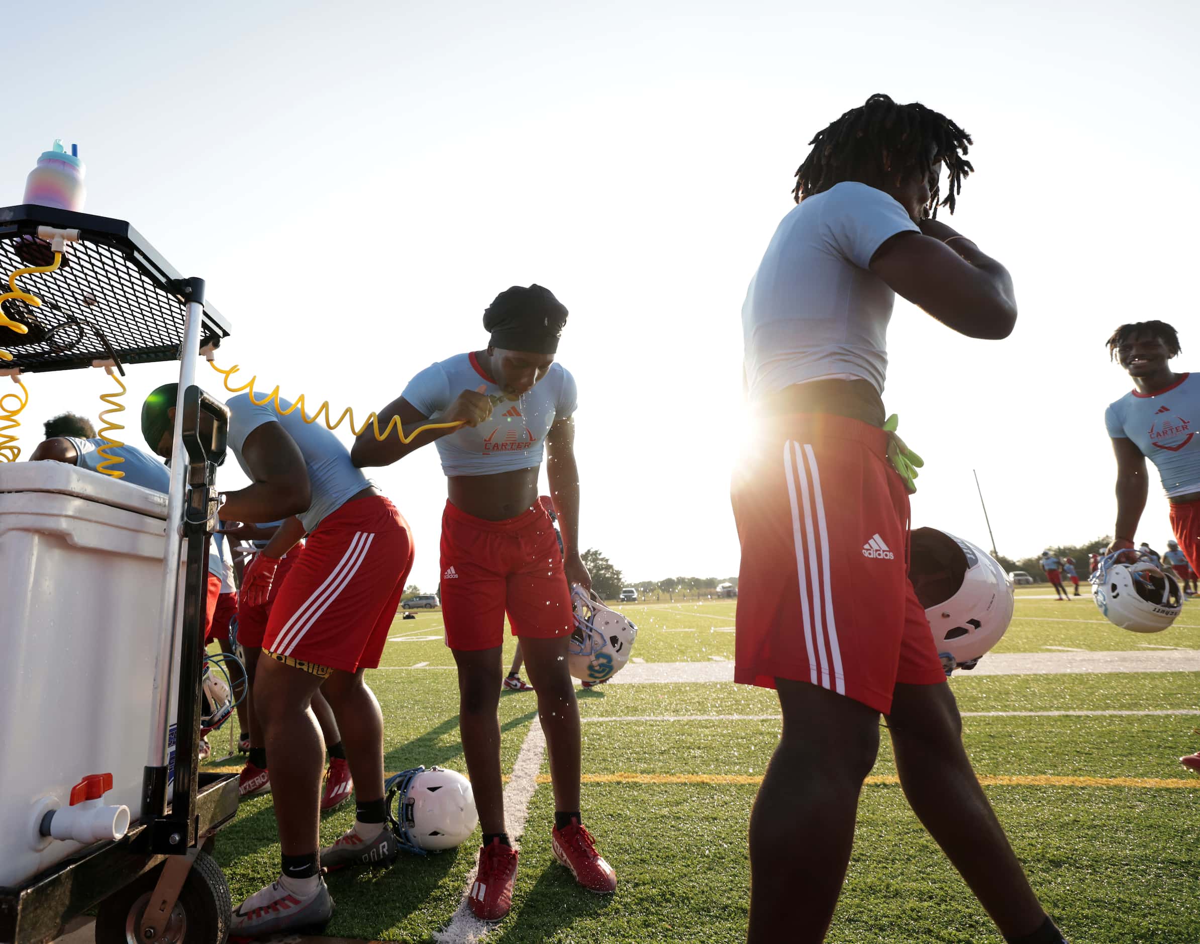 Players get a drink as they attend their first day of football practice at Carter High...