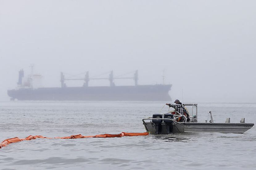 A boat tows an oil containment boom into the Houston Ship Channel Monday as a cargo ship...