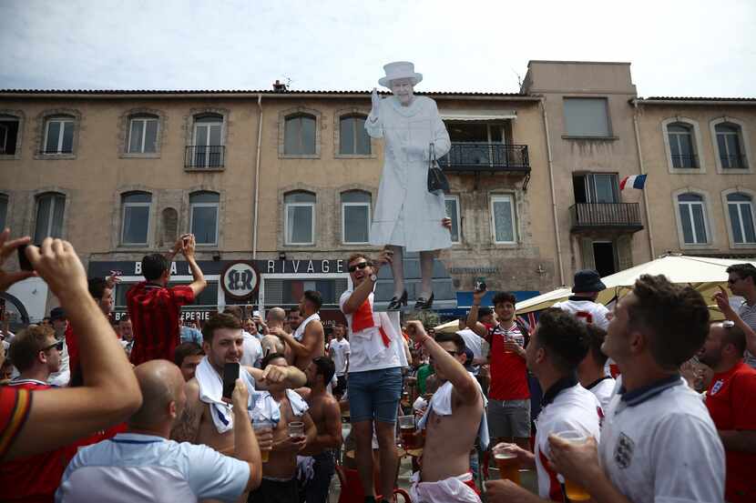  England fans hold up a cardboard figure of Queen Elizabeth II as they gather and cheer...