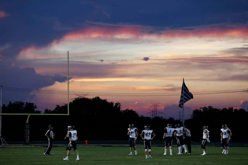 Jesuit players wait for the play to resume as the sun sets during a high school football...