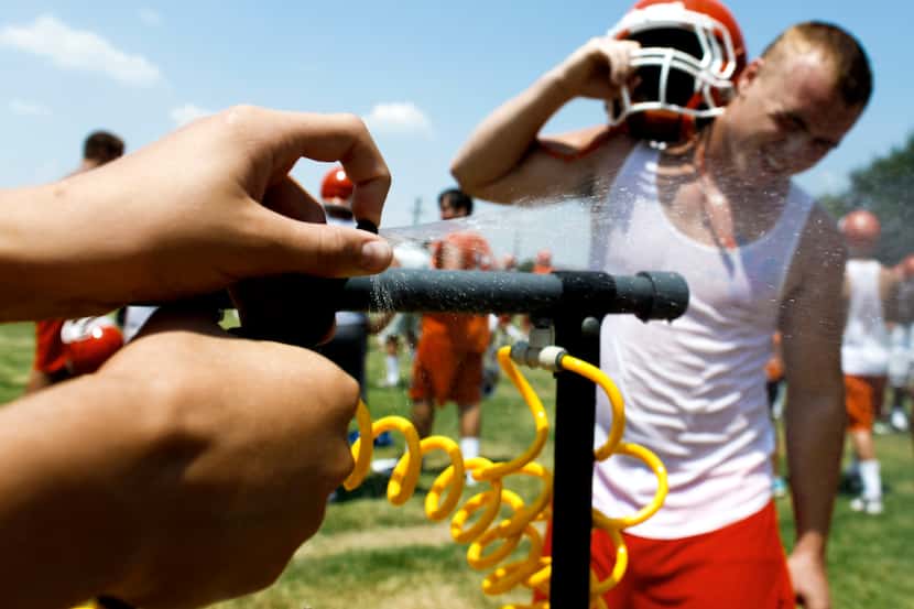 Celina High School football manager Kyle Thile sprays water on Reece Morton during a...