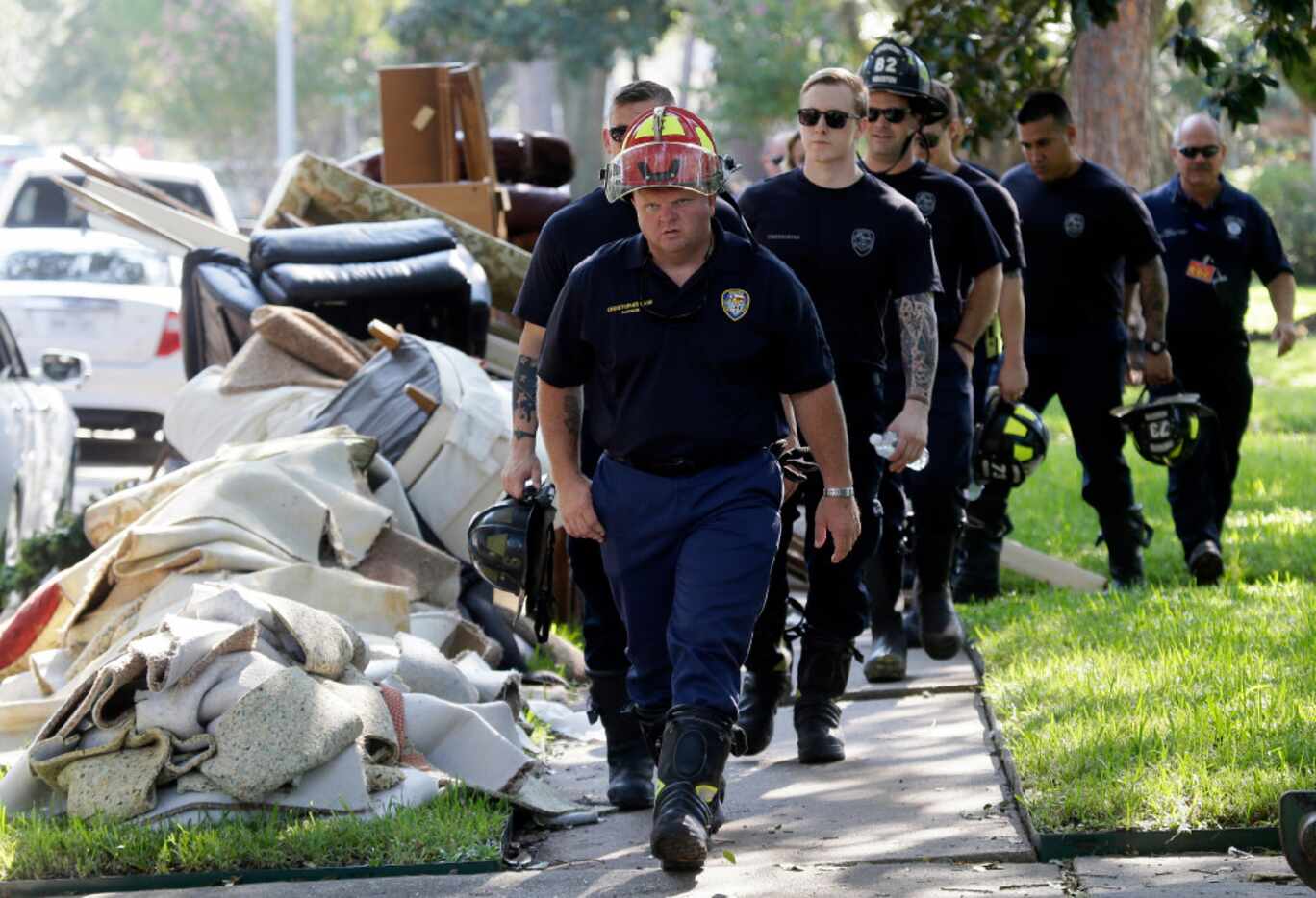 Firefighters walk around debris removed from homes during a door-to-door survey of a...