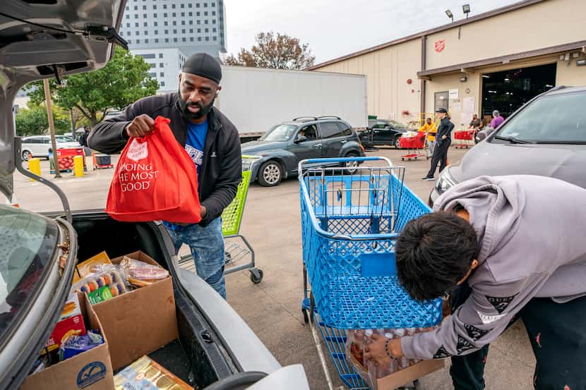 Volunteers Andre Brown, left, and John Rodriguez load groceries into the trunk of a car...