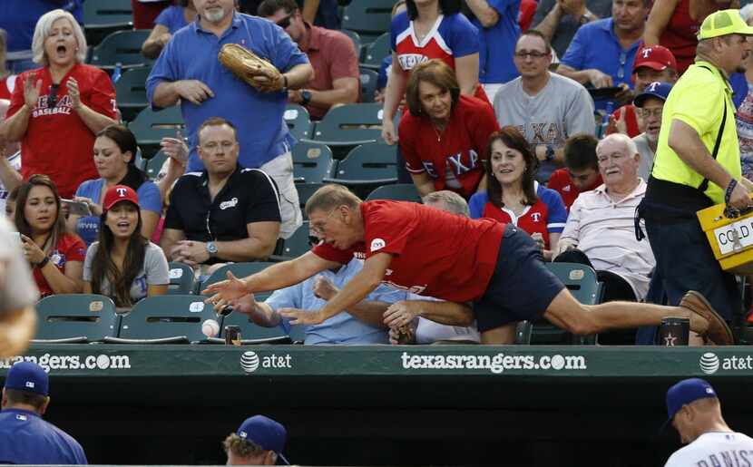 A Texas Rangers fan dives for a ball on the dugout in front of other fans during a break in...