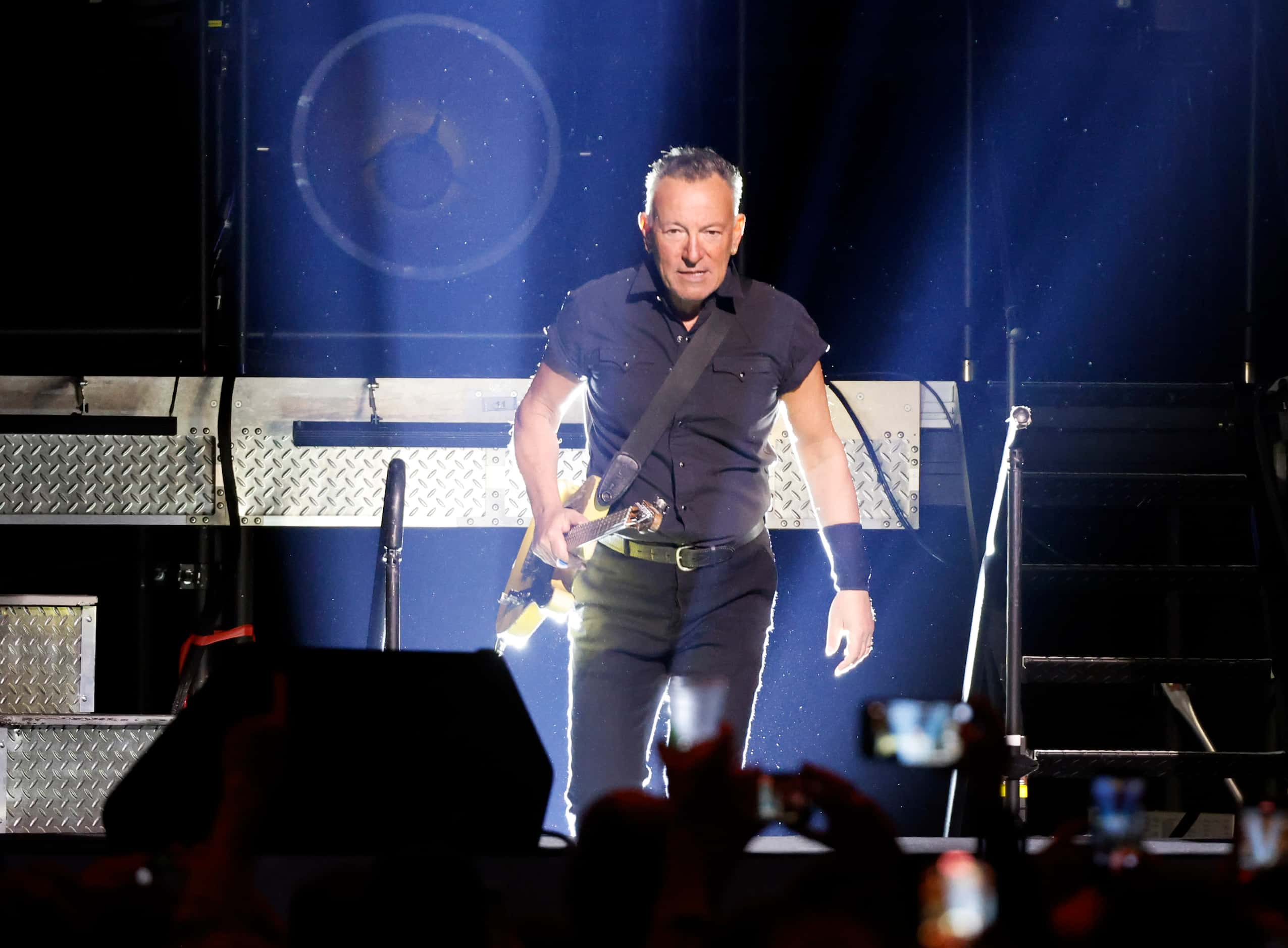 Clad in a black pearl snap shirt and black pants, Bruce Springsteen walks to the stage...