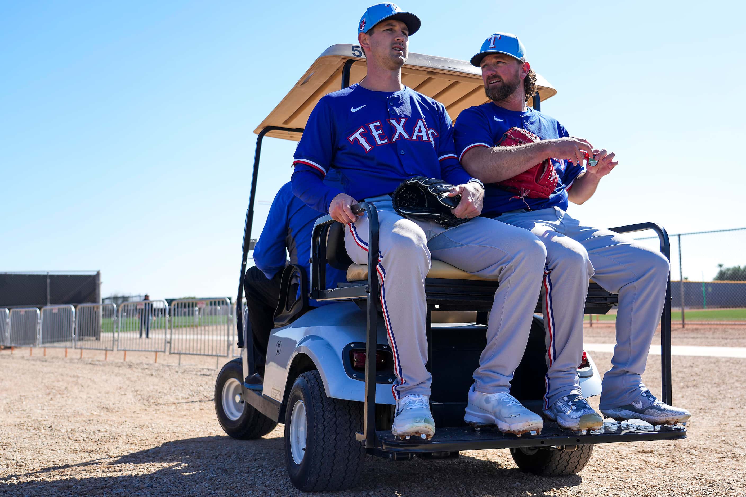 Texas Rangers pitchers Tyler Mahle (left) and Kirby Yates ride in a golf cart between drills...