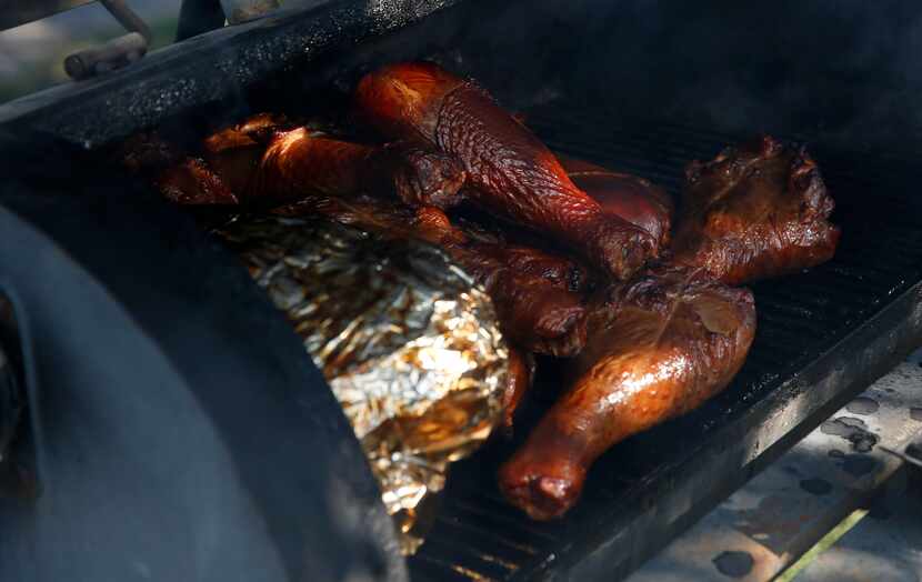 Wrapped brisket sits beside turkey legs on the barbecue pit tended by Stacey Walker on...