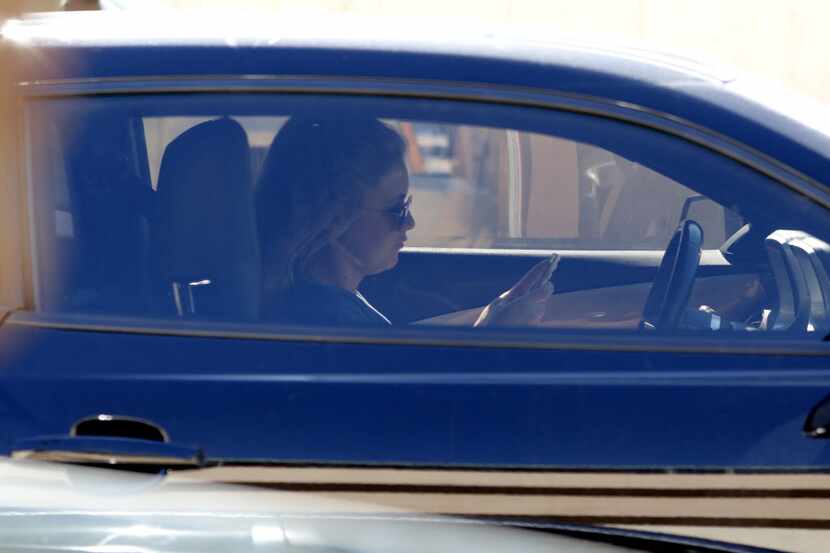 A women looks at her phone while driving down Central Expressway in Dallas on July 16, 2015....
